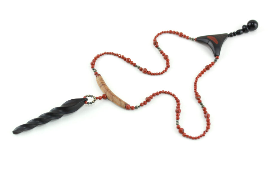 Choker design en bois exotiques & Jaspe rouge, avec pour pendentif une vrille en bois d'ébène noir, attachée par un cercle de petite perle de pyrité bronze doré scintillant, reliée à une pièce balancelle courbée en bois d'olivier crème foncé boisé, et un fil de perles rouge brique ponctués de deux de pyrite partent des deux côté de la pièce jusqu'au fermoir puzzle aimanté de forme triangulaire, avec un pendant de perles noires en fermeture