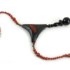 Design-Choker aus exotischen Hölzern und rotem Jaspis, mit einer Ranke aus schwarzem Ebenholz als Anhänger, die mit einem Kreis aus kleinen, glitzernden, goldbronzenen Pyritperlen befestigt ist, verbunden mit einem gebogenen Schaukelstück aus dunkel cremefarbenem, holzigem Olivenholz, und einer Perlenschnur aus ziegelroten, mit zwei Pyritperlen punktierten Perlen, die von beiden Seiten des Stücks zu einem dreieckigen, magnetischen Puzzle-Verschluss mit einem Anhänger aus schwarzen Perlen als Verschluss führt.