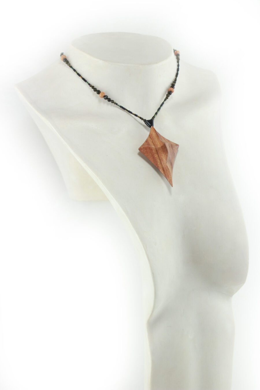 Collier croix primitive en bois : collier de perles noires, orange et vert métallisé fermé par un fermoir aimanté. Pendentif en forme de croix, bombée vers le haut, avec des lignes qui dessinent une croix sinueuse