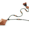 Collier croix primitive en bois : collier de perles noires, orange et vert métallisé fermé par un fermoir aimanté. Pendentif en forme de croix, bombée vers le haut, avec des lignes qui dessinent une croix sinueuse