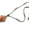 Collier croix primitive en bois : collier de perles noires, orange et vert métallisé fermé par un fermoir aimanté. Pendentif en forme de croix, bombée vers le haut, avec des lignes qui dessinent une croix sinueuse