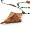 Collier croix primitive en bois : collier de perles noires, orange et vert métallisé fermé par un fermoir aimanté. Pendentif en forme de croix, bombée vers le haut, avec des lignes qui dessinent une croix sinueuse