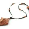 Collier croix primitive en bois : collier de perles noires, orange et vert métallisé fermé par un fermoir aimanté. Pendentif en forme de croix, bombée vers le haut, avec des lignes qui dessinent une croix sinueuse