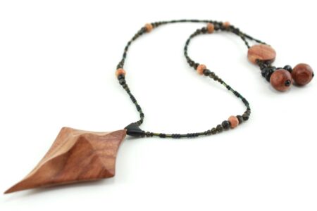 Collier croix primitive en bois : collier de perles noires, orange et vert métallisé fermé par un fermoir aimanté. Pendentif en forme de croix, bombée vers le haut, avec des lignes qui dessinent une croix sinueuse