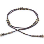 un collier lariat sensuel en perles naturelles de Bronzite et perles noires avec des touches dorées et marron qui se termine par deux cristaux de couleur ambre