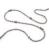 un collier lariat sensuel en perles naturelles de Bronzite et perles noires avec des touches dorées et marron qui se termine par deux cristaux de couleur ambre