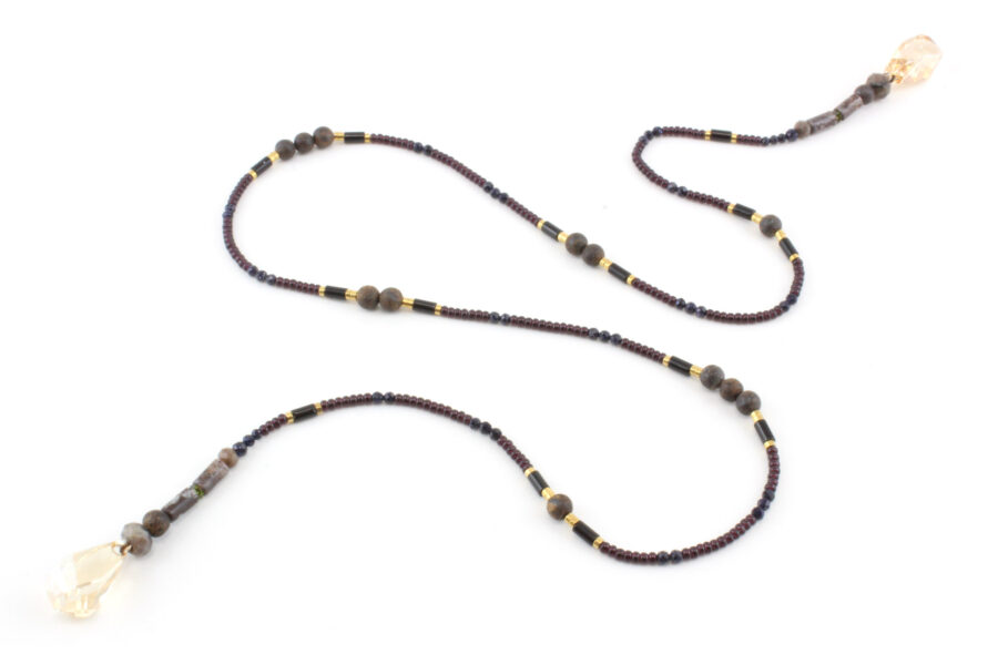 un collier lariat sensuel en perles naturelles de Bronzite et perles noires avec des touches dorées et marron qui se termine par deux cristaux de couleur ambre