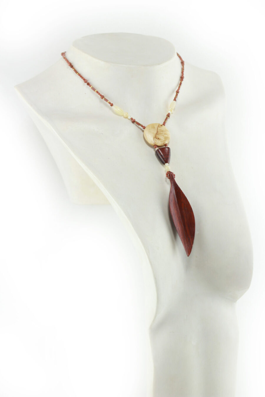 Princesse Padouk à Calcite, avec pour pendentif une feuille élancée en bois orange foncé, un disque crème boisé, un collier de perles orange foncé avec des touches de crème et un fermoir puzzle aimanté qui se termine par un double pendant de perles