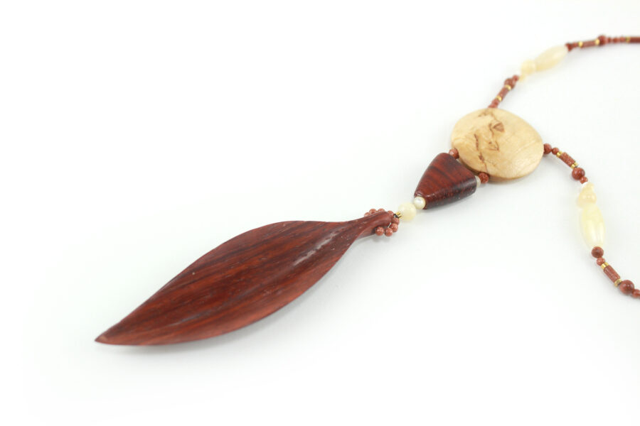 Princesse Padouk à Calcite, avec pour pendentif une feuille élancée en bois orange foncé, un disque crème boisé, un collier de perles orange foncé avec des touches de crème et un fermoir puzzle aimanté qui se termine par un double pendant de perles