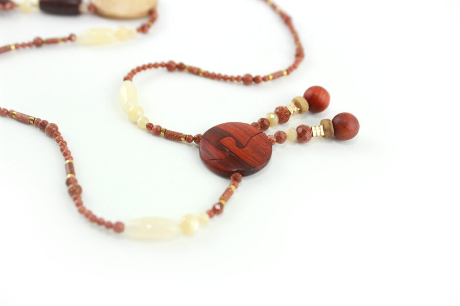 Princesse Padouk à Calcite, avec pour pendentif une feuille élancée en bois orange foncé, un disque crème boisé, un collier de perles orange foncé avec des touches de crème et un fermoir puzzle aimanté qui se termine par un double pendant de perles