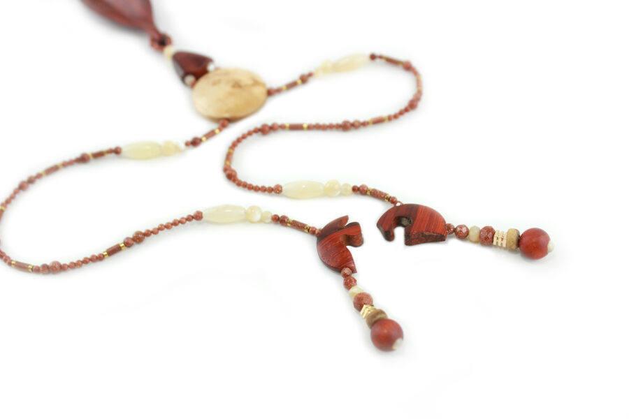 Princesse Padouk à Calcite, avec pour pendentif une feuille élancée en bois orange foncé, un disque crème boisé, un collier de perles orange foncé avec des touches de crème et un fermoir puzzle aimanté qui se termine par un double pendant de perles