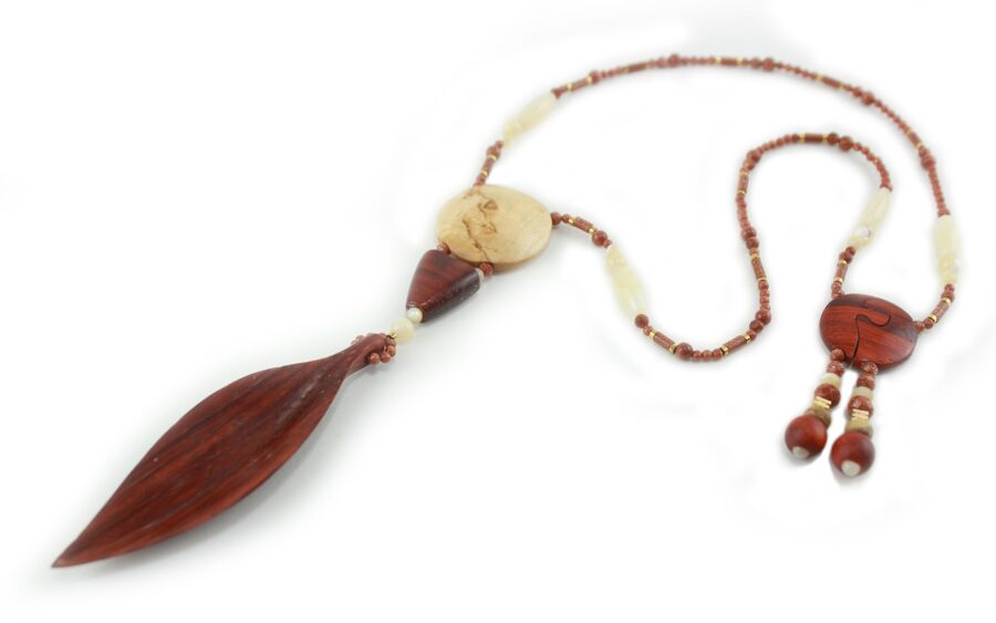 Princesse Padouk à Calcite, avec pour pendentif une feuille élancée en bois orange foncé, un disque crème boisé, un collier de perles orange foncé avec des touches de crème et un fermoir puzzle aimanté qui se termine par un double pendant de perles