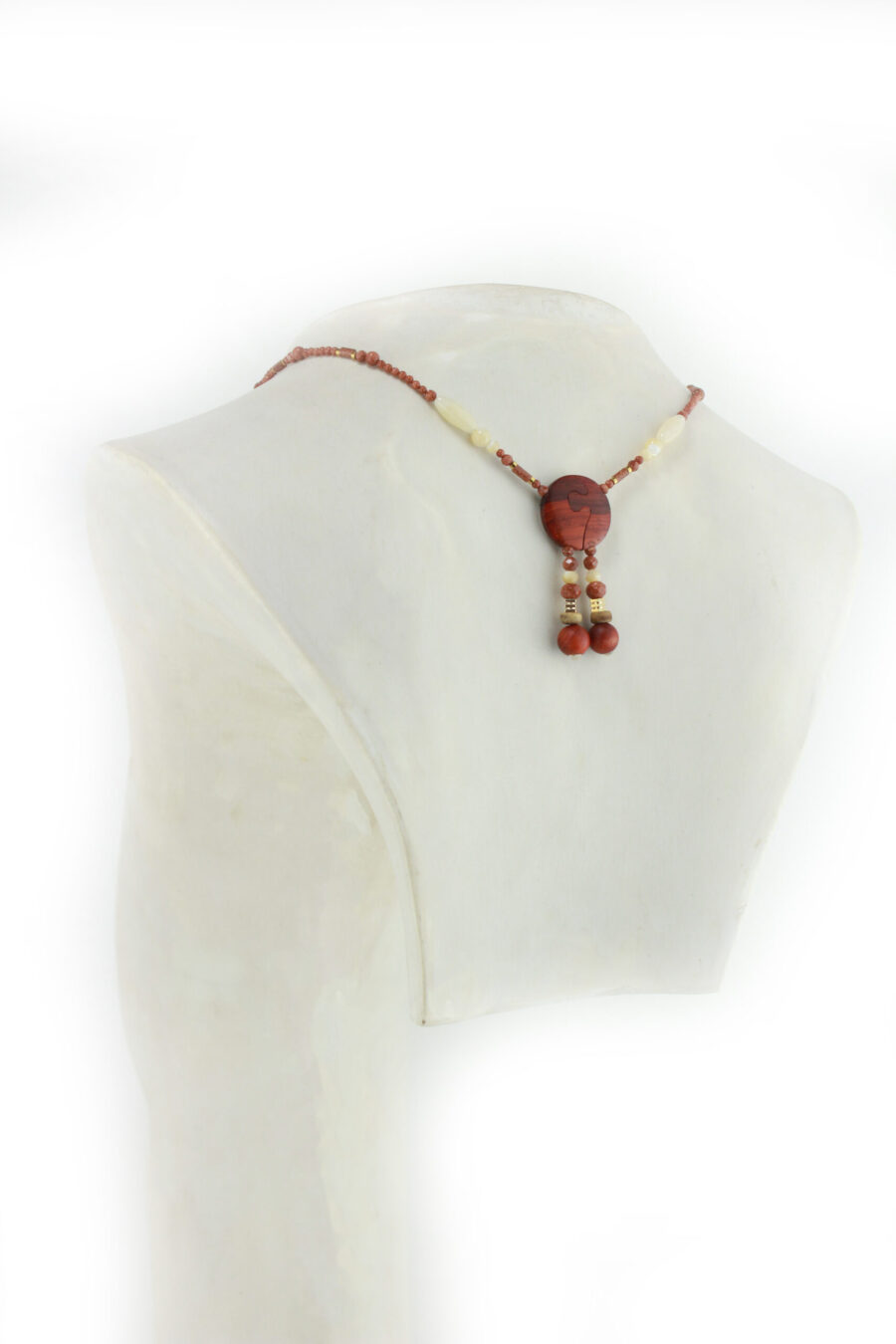 Princesse Padouk à Calcite, avec pour pendentif une feuille élancée en bois orange foncé, un disque crème boisé, un collier de perles orange foncé avec des touches de crème et un fermoir puzzle aimanté qui se termine par un double pendant de perles