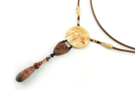 Collier sautoir en bois de Bouleau Madré sculpté & Picasso, avec en pendentif un disque crème boisé, une petite pièce en bois bombée marron tachetée de noir, une suite de perles et une pierre sculptée en forme d'olive vert tacheté d'orange. Cordon de cuir couleur camel relié aux pendant avec deux pièces de bois sculpté en forme d'olive