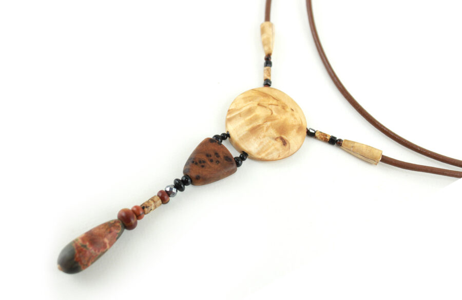 Collier sautoir en bois de Bouleau Madré sculpté & Picasso, avec en pendentif un disque crème boisé, une petite pièce en bois bombée marron tachetée de noir, une suite de perles et une pierre sculptée en forme d'olive vert tacheté d'orange. Cordon de cuir couleur camel relié aux pendant avec deux pièces de bois sculpté en forme d'olive