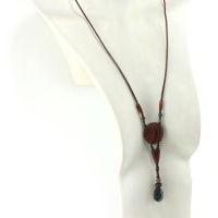 Halskette aus exotischem Holz und Obsidianstein. Als Anhänger eine dunkelorangefarbene Scheibe mit schwarzem Zebramuster, ein kleines, dunkelorangefarbenes, gewölbtes Holzstück, eine Reihe von Perlen und ein khakigrüner, geschnitzter, tropfenförmiger Stein. Dunkelbraune Lederkordel, die mit zwei olivenförmigen geschnitzten Holzstücken an den Anhängern befestigt ist.