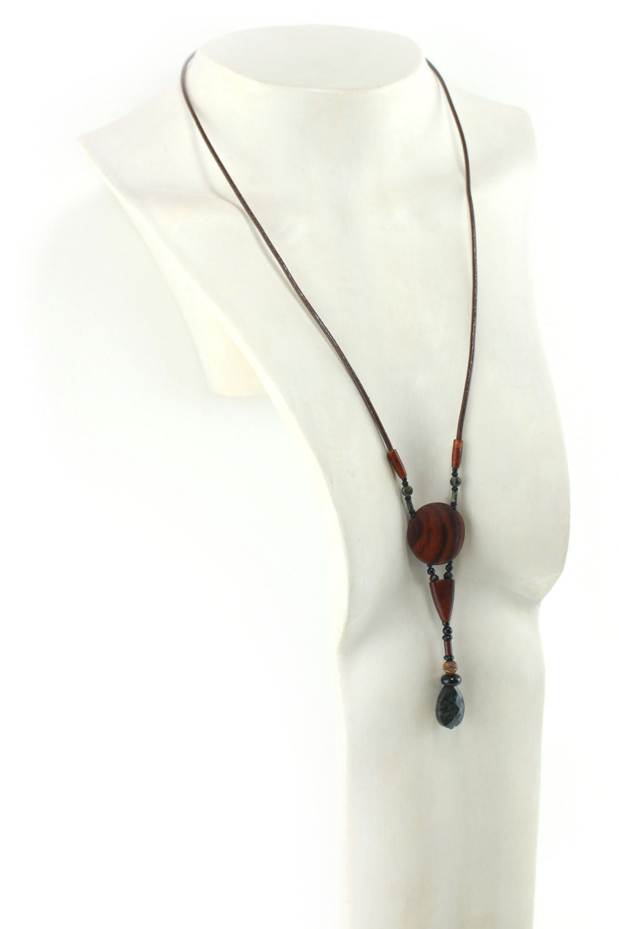 Halskette aus exotischem Holz und Obsidianstein. Als Anhänger eine dunkelorangefarbene Scheibe mit schwarzem Zebramuster, ein kleines, dunkelorangefarbenes, gewölbtes Holzstück, eine Reihe von Perlen und ein khakigrüner, geschnitzter, tropfenförmiger Stein. Dunkelbraune Lederkordel, die mit zwei olivenförmigen geschnitzten Holzstücken an den Anhängern befestigt ist.