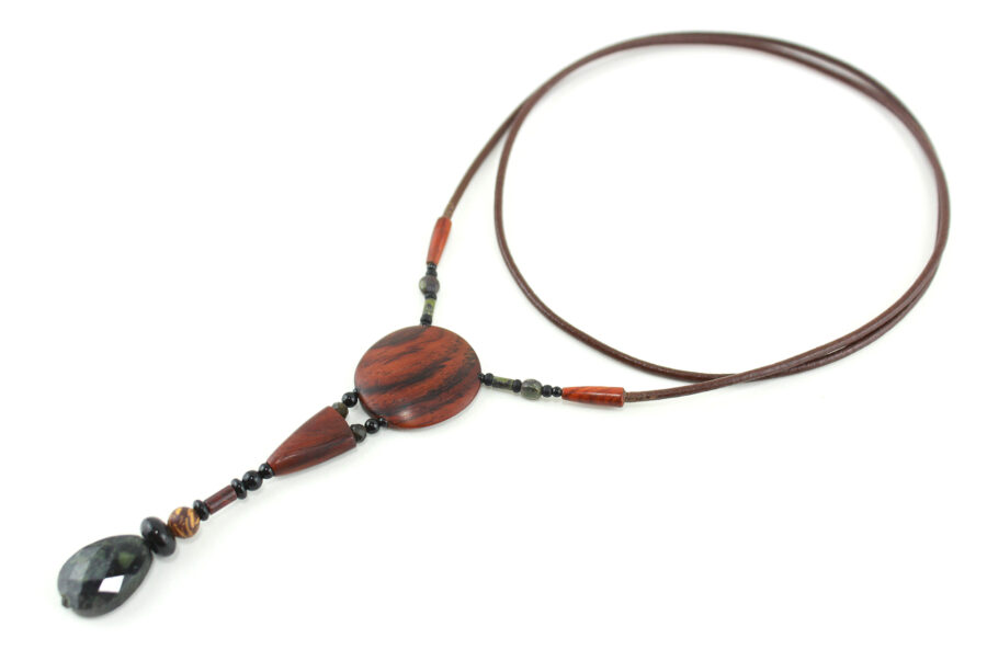 Sautoir en bois exotique et pierre d'Obsidienne, avec en pendentif un disque orange foncé zébré de noir, une petite pièce en bois bombée orange foncé, une suite de perles et une pierre sculptée en forme de goutte vert kaki. Cordon de cuir marron foncé relié aux pendant avec deux pièces de bois sculpté en forme d'olive