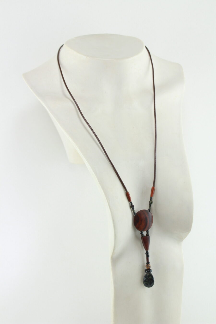 Sautoir en bois exotique et pierre d'Obsidienne, avec en pendentif un disque orange foncé zébré de noir, une petite pièce en bois bombée orange foncé, une suite de perles et une pierre sculptée en forme de goutte vert kaki. Cordon de cuir marron foncé relié aux pendant avec deux pièces de bois sculpté en forme d'olive