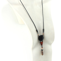 Collar tótem de maderas exóticas y jaspe Picasso, con un colgante formado por un disco de ébano negro, una pequeña pieza curvada de madera de color naranja oscuro, una serie de perlas y una piedra tallada en forma de aceituna verde moteada de naranja. Cordón de cuero negro unido al colgante con dos piezas de madera tallada en forma de aceituna.