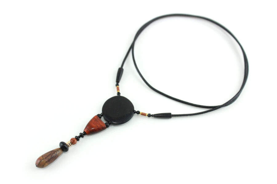 Collier totem en bois exotiques et Jaspe Picasso, avec en pendentif un disque noir ébène, une petite pièce en bois bombée orange foncé, une suite de perles et une pierre sculptée en forme d'olive vert tacheté d'orange. Cordon de cuir noir relié aux pendant avec deux pièces de bois sculpté en forme d'olive