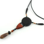 Collier totem en bois exotiques et Jaspe Picasso, avec en pendentif un disque noir ébène, une petite pièce en bois bombée orange foncé, une suite de perles et une pierre sculptée en forme d'olive vert tacheté d'orange. Cordon de cuir noir relié aux pendant avec deux pièces de bois sculpté en forme d'olive