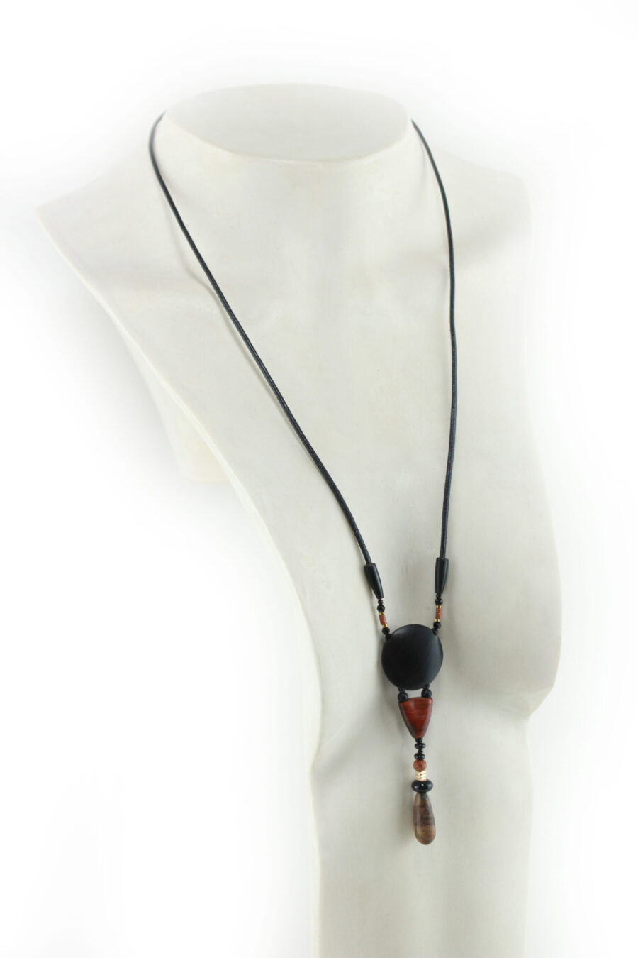 Collier totem en bois exotiques et Jaspe Picasso, avec en pendentif un disque noir ébène, une petite pièce en bois bombée orange foncé, une suite de perles et une pierre sculptée en forme d'olive vert tacheté d'orange. Cordon de cuir noir relié aux pendant avec deux pièces de bois sculpté en forme d'olive