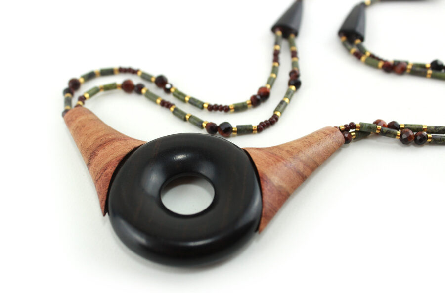 Ras-de-cou artisanal en bois naturel d'Ebène, avec un cercle donuts noir, deux pièces en bois orange qui l'encadrent vers le haut du cercle, deux ranges de perles les prolongent jusqu'à deux pièces en bois intermédiaires qui font le lien avec le fermoir puzzle aimanté noir