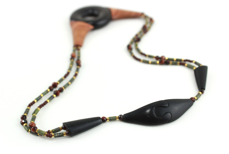 Ras-de-cou artisanal en bois naturel d'Ebène, avec un cercle donuts noir, deux pièces en bois orange qui l'encadrent vers le haut du cercle, deux ranges de perles les prolongent jusqu'à deux pièces en bois intermédiaires qui font le lien avec le fermoir puzzle aimanté noir