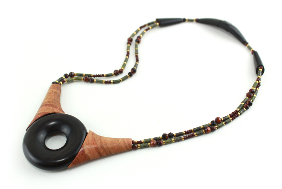 Ras-de-cou artisanal en bois naturel d'Ebène, avec un cercle donuts noir, deux pièces en bois orange qui l'encadrent vers le haut du cercle, deux ranges de perles les prolongent jusqu'à deux pièces en bois intermédiaires qui font le lien avec le fermoir puzzle aimanté noir