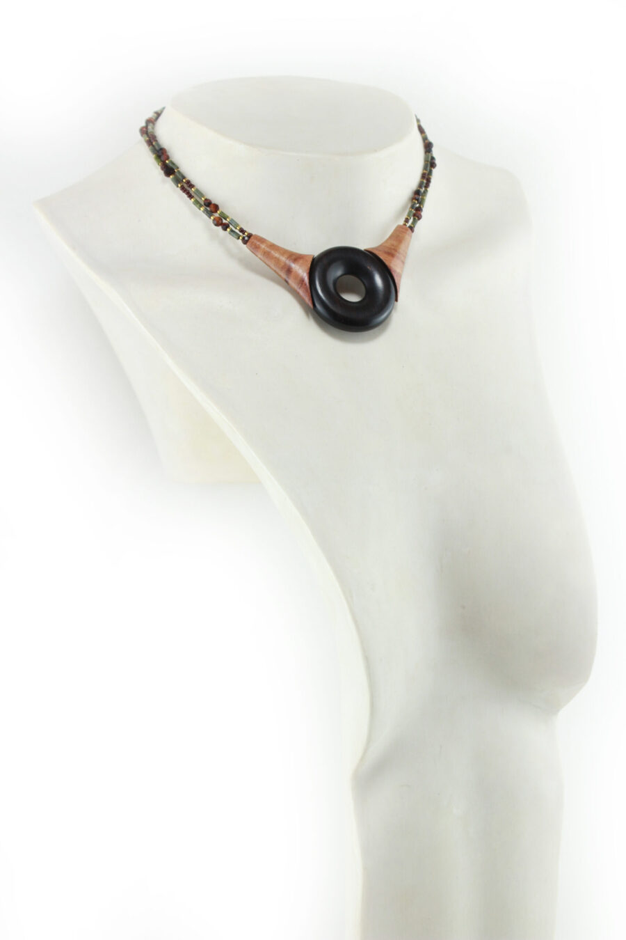 Ras-de-cou artisanal en bois naturel d'Ebène, avec un cercle donuts noir, deux pièces en bois orange qui l'encadrent vers le haut du cercle, deux ranges de perles les prolongent jusqu'à deux pièces en bois intermédiaires qui font le lien avec le fermoir puzzle aimanté noir