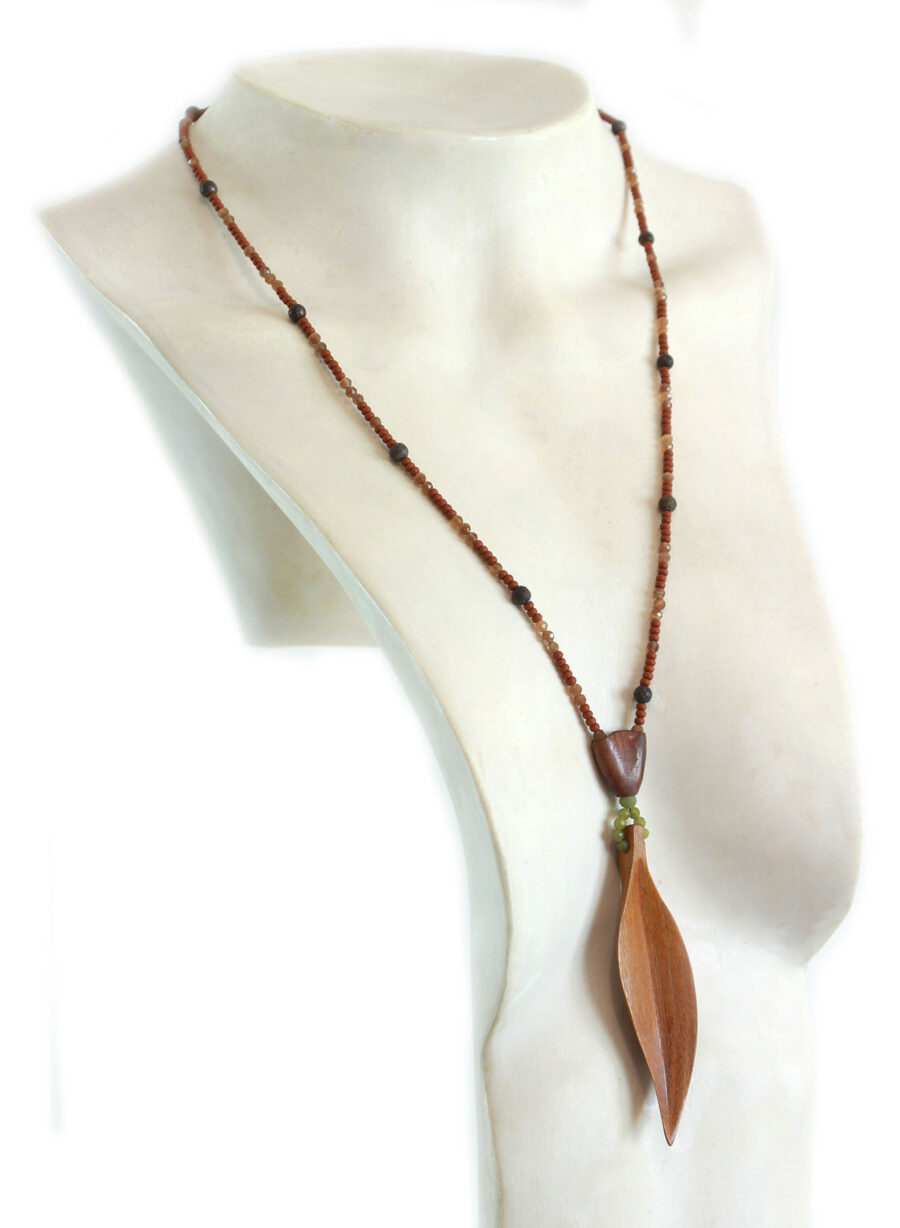 Sautoir-en-Bois-exotique-perles-naturelles avec une feuille élancée jaune en pendant, reliée à un cercle de perles vertes et une petite pièce en bois bombée d'où part la partie suite de perle. Collier sautoir long, la feuille arrive au creux de la poitrine