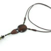 Sautoir en bois sculpté & perles naturelles : cordon en cuir avec pendant ethnique, un cercle sculpté en bois marron relié par des perles noires à une pièce en bois bombée marron, reliée à une suite de perles qui se terminent par une pierre verte d'Unakite