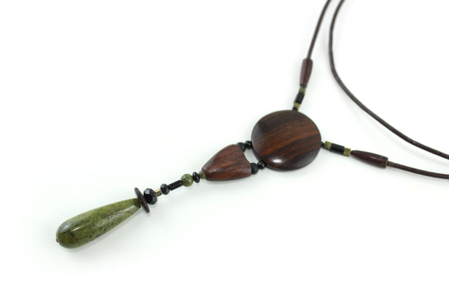 Sautoir en bois sculpté & perles naturelles : cordon en cuir avec pendant ethnique, un cercle sculpté en bois marron relié par des perles noires à une pièce en bois bombée marron, reliée à une suite de perles qui se terminent par une pierre verte d'Unakite