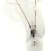 Collana lunga magnetica in Ziricote e Diaspro Dalmata, con un pendente a forma di disco zebrato grigio nero, un piccolo pezzo di legno a cupola marrone scuro, una serie di perle e una pietra intagliata a forma di goccia bianca punteggiata di nero. Il cordone di cuoio arancione dorato è collegato al ciondolo con due pezzi di legno intagliato a forma di oliva.