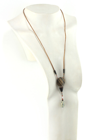 Sautoir magnétique en Ziricote & Jaspe dalmatien, avec en pendentif un disque noir grisé zébré, une petite pièce en bois bombée marron foncé, une suite de perles et une pierre sculptée en forme de goutte blanche tachetée de noir. Cordon de cuir orange doré relié aux pendant avec deux pièces de bois sculpté en forme d'olive
